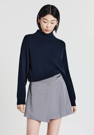 Marineblaues Rollkragenpullover kombiniert mit einem hellgrauen Wickelrock, der über eine seitliche Schnalle verfügt, aus glattem Stoff und mit einem gefalteten Design.