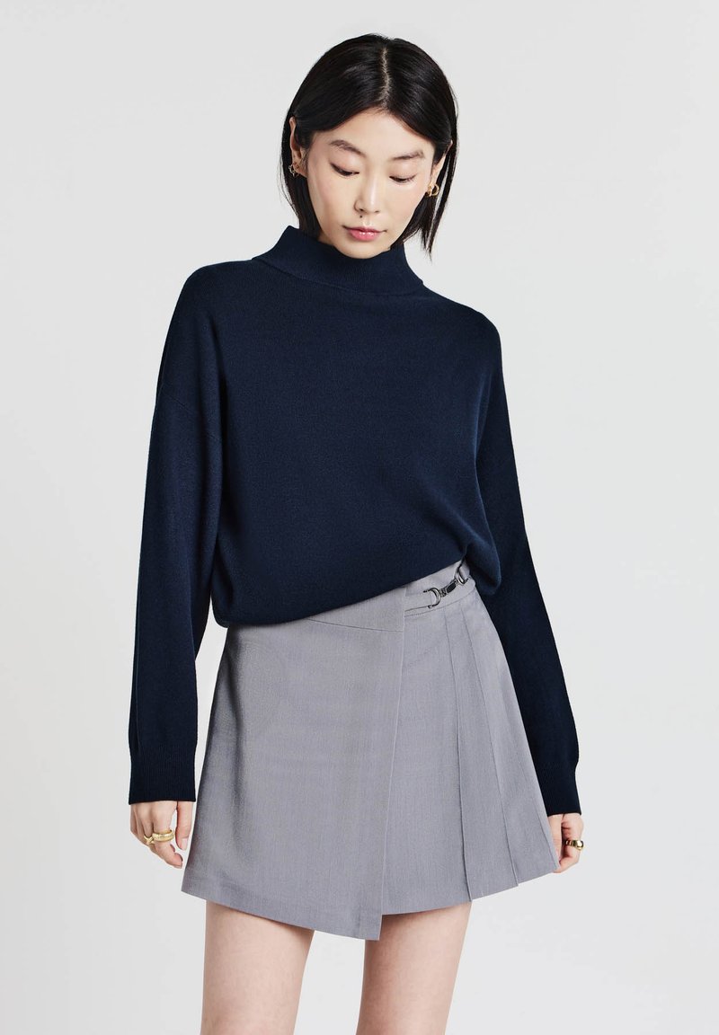 Maglione a collo alto blu navy abbinato a una gonna a portafoglio grigia chiara con fibbia laterale, tessuto morbido e design plissettato.