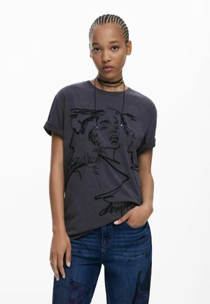 Black graphic T-shirt featuring a stylized female portrait, round neckline, rolled sleeves, and soft cotton fabric; paired with blue jeans.