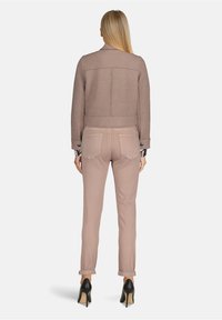 Jasnoróżowa dopasowana marynarka o teksturowanym wykończeniu, krótki fason i dwie tylne kieszenie. W komplecie z jasnoróżowymi spodniami w rolce i czarnymi szpilkami.
