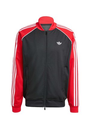 Chaqueta de malla negra con mangas rojas, con tres rayas blancas en cada manga y un pequeño logo blanco en el pecho. Cierre de cremallera.