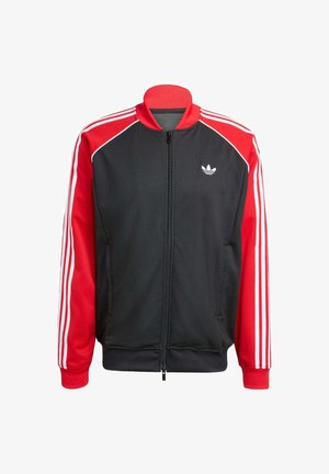 Zwarte mesh jas met rode mouwen, voorzien van drie witte strepen op elke mouw en een klein wit logo op de borst. Ritssluiting.