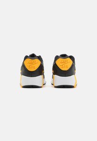 Fekete és sárga Nike Air sportcipők, texturált felsőrész, fehér középtalppal és jellegzetes logóval a saroknál. Lekerekített forma, párnázott bokarésze van.