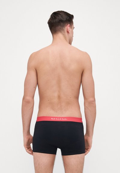 Boxer shorts noirs avec une ceinture élastique rouge comportant du texte blanc. Les shorts ont une coupe ajustée et une texture lisse et douce.