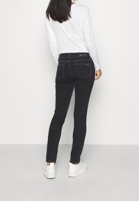 Jeans negros ajustados con una cinturilla normal, bolsillos traseros y detalles de costura sutiles, combinados con una camiseta blanca de manga larga y zapatillas blancas.