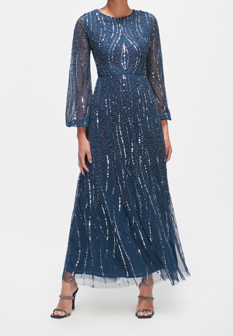 Lång mörkblå klänning med genomskinliga långa ärmar, prydad med silverfärgade paljetter som liknar vertikala ränder. Lätt fallande tyg, ankle-length.