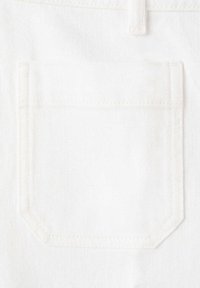Tissu denim blanc avec une poche rectangulaire cousue présentant des coins inférieurs biseautés et une texture visible.