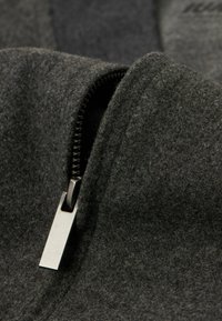 Donkergrijze viltstof met een close-up van de textuur, featuring een zilveren metalen rits die gedeeltelijk geopend is, waardoor de zachtheid van het materiaal benadrukt wordt.