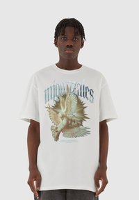 Baltas per didelis T-shirt su dviej�ų balandžių grafika ir stilizuotu tekstu. Spauda apima švelnias spalvas ir puošnius detales.