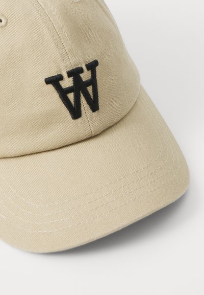Beige cotton baseball cap with a curved bill. Features a black embroidered "W" logo on the front and standard stitching patterns.