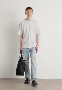Hvid oversized t-shirt, lyseblå slidte jeans, sort tote bag og sorte sko. Simpelt design med en afslappet pasform og synlige huller.