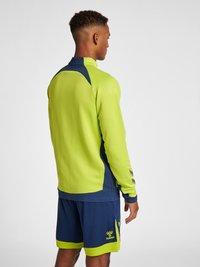 Zielona sportowa bluza z kapturem z granatowymi akcentami; teksturowana górna część pleców i rękawy; logo na dolnej lewej części. Noszona z pasującymi granatowymi szortami.