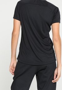 Czarny sportowy top z krótkimi rękawami, lekko luźnym krojem i gładką fakturą, zestawiony z dopasowanymi czarnymi spodniami.