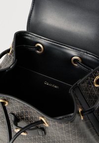 Μαύρη δερμάτινη τσάντα τύπου πουγκί με χρυσά μεταλλικά στοιχεία, που διαθέτει εξωτερική επιφάνεια με μοτίβο και εσωτερική ετικέτα με την επιγραφή "Calvin Klein".