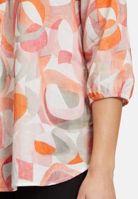 Ihanteen, kevyt paita, jossa on värikäs geometrinen kuvio vaaleanpunaisen, oranssin, harmaan ja valkoisen sävyissä. Varustettu 3/4-hiisilla, joissa on joustavat hihansuut.