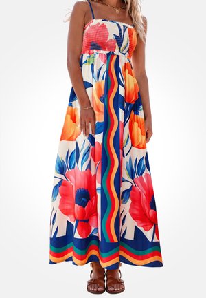Femme portant une robe longue bustier colorée avec de grandes fleurs rouges et orange ainsi que des rayures verticales ondulées bleu, vert et rouge, assortie à des sandales marron.