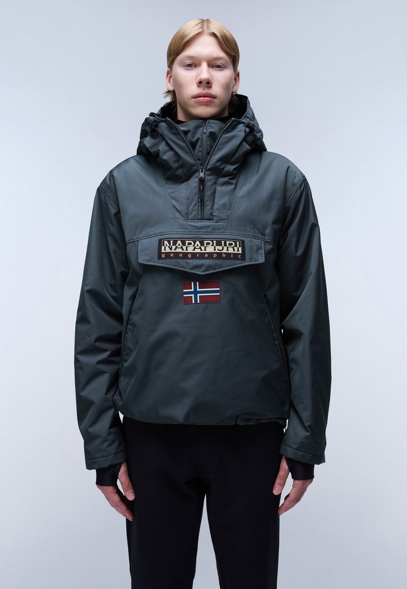 Tummanvihreä kevyt takki, jossa on korkea kaulus, vetoketjulla varustettu etuosa, iso vaakasuuntainen logo-patch ja pieni Norjan lipun yksityiskohta.