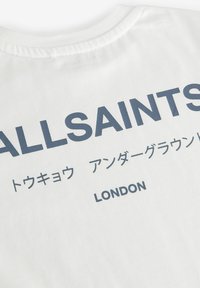 Bílá bavlněná trička s tmavě modrým textem, na kterém je "ALLSAINTS" a japonské znaky, a na spodní části je "LONDON". Krátký rukáv.