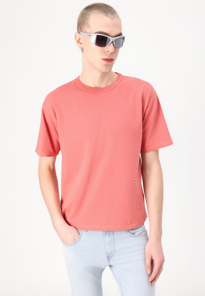 Korallefarbene Baumwoll-T-Shirt mit kurzen Ärmeln und Rundhalsausschnitt, kombiniert mit hellblauen Jeans aus Denim, die ein dezentes Logodetail aufweisen.