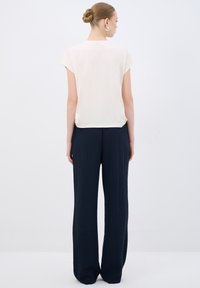 Haut créme pour femmes à manches courtes, associé à un pantalon large bleu marine, avec un tissu texturé et une silhouette décontractée.