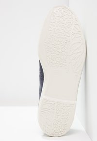 Temno modra obutev z teksturirano gumijasto podplatom v beli barvi, ki ima zapletene vzorce in oznako velikosti 37. Izdelano v Španiji.