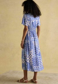 Blaue und weiße gemusterte Midi-Kleid mit kurzen Ärmeln, tailliertem Schnitt und floralen Designs. Tragen mit einfachen beigen Sandalen.