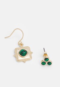 Brincos em tom dourado com um design de gota quadrada, apresentando uma pedra verde e uma argola com três pedras verdes menores.
