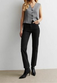 Top gris sin mangas con escote en V y botones, combinado con pantalones negros de pierna recta de talle alto y botas de tobillo negras con punta.