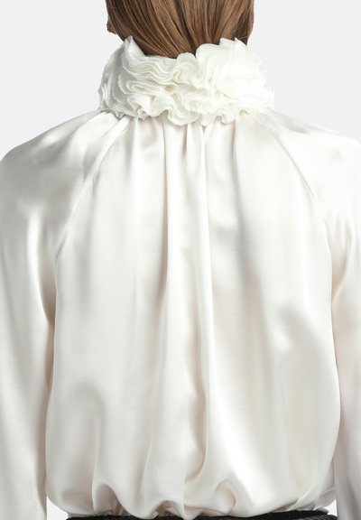 Blusa di raso bianca con colletto arricciato e design posteriore fluido, con delicata lucentezza e morbida consistenza.