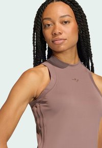Jasnofioletowy bezrękawnik sportowy z wysokim dekoltem, z prążkowymi detalami po bokach i wytłoczonym logo na piersi. Gładka tekstura materiału.