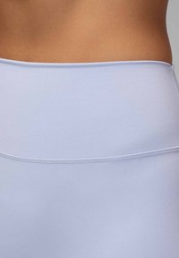 Sección media de una persona que lleva leggings deportivos de tiro alto de color lavanda claro con costuras suaves y sin costuras visibles.