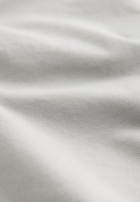 Gros plan sur un tissu blanc doux et lisse avec une subtile texture côtelée diagonale et de légers plis créant des variations de lumière et d'ombre.