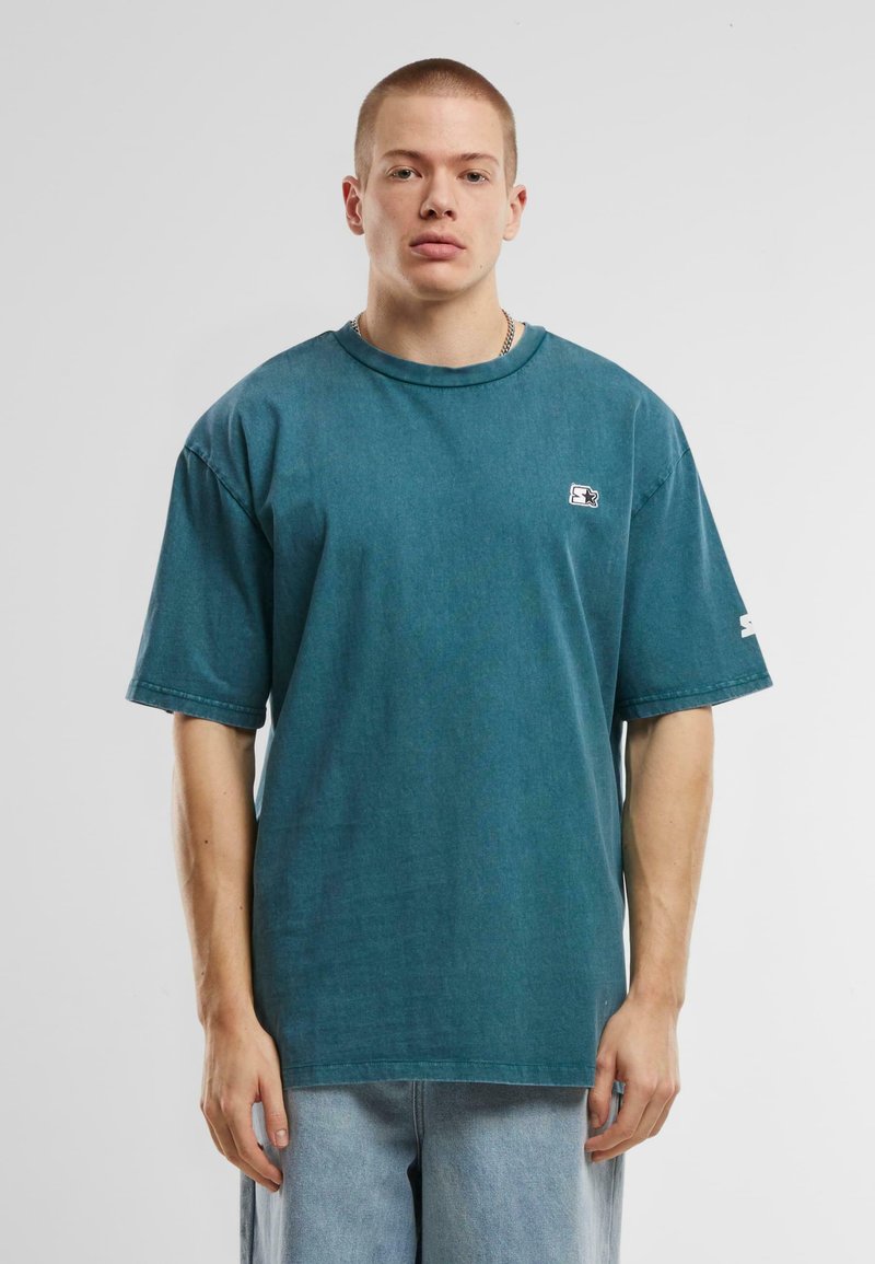 T-shirt surdimensionné en coton turquoise, à manches courtes, col rond côtelé, petite patch de marque sur la poitrine et accents de couture.