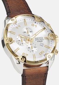 Montre chronographe argent et or avec un cadran blanc, un bracelet en cuir brun, un grand boîtier rond et de grands index d'heure et sous-cadrans.