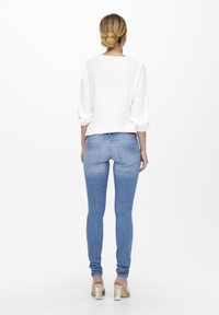 Jeans ajustados de color azul claro con una textura suave, combinados con una blusa blanca de corte holgado y de manga larga. La blusa tiene un escote amplio.