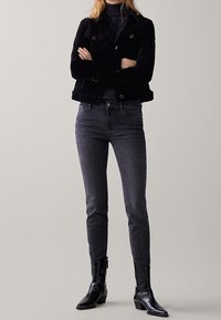 Musta verryttelytakki, jossa kaksi etutaskua, yhdistetty tummanharmaisiin slim-fit-farkkuihin. Täydennetty kiiltävillä mustilla nilkkureilla.