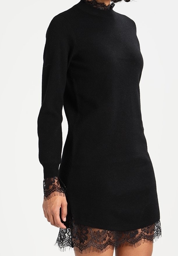 Svart stickad klänning med långa ärmar, med hög hals och spetsdetaljer vid ärmarna och fåll, vilket skapar en lagertextur.