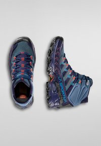 Buty trekkingowe w niebieskiej i granatowej siatce z pomarańczowymi akcentami, teksturowana cholewka i wytrzymała czarna podeszwa. Charakteryzują się wzmocnioną osłoną palców i sznurówkami.