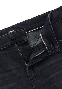 Dunkelblaue Jeans mit Reißverschluss, Knopfverschluss und Logohänger. Sie besitzen eine glatte Textur und kontrastierende Nähte entlang der Taschen.