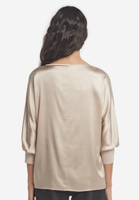 Beżowa satynowa bluzka o luźnym kroju, z szerokim dekoltem i bufkami o długości do połowy ramienia. Gładka struktura z delikatnym połyskiem.