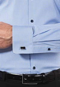 Camicia a quadri blu e bianca con bottoni neri, polsini alla francese e gemelli neri. Il tessuto appare liscio con una texture croccante.