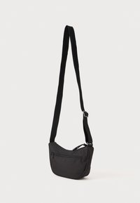 Black fabric shoulder bag with a curved shape, adjustable strap, and a front zip pocket. Smooth texture with minimalist design.