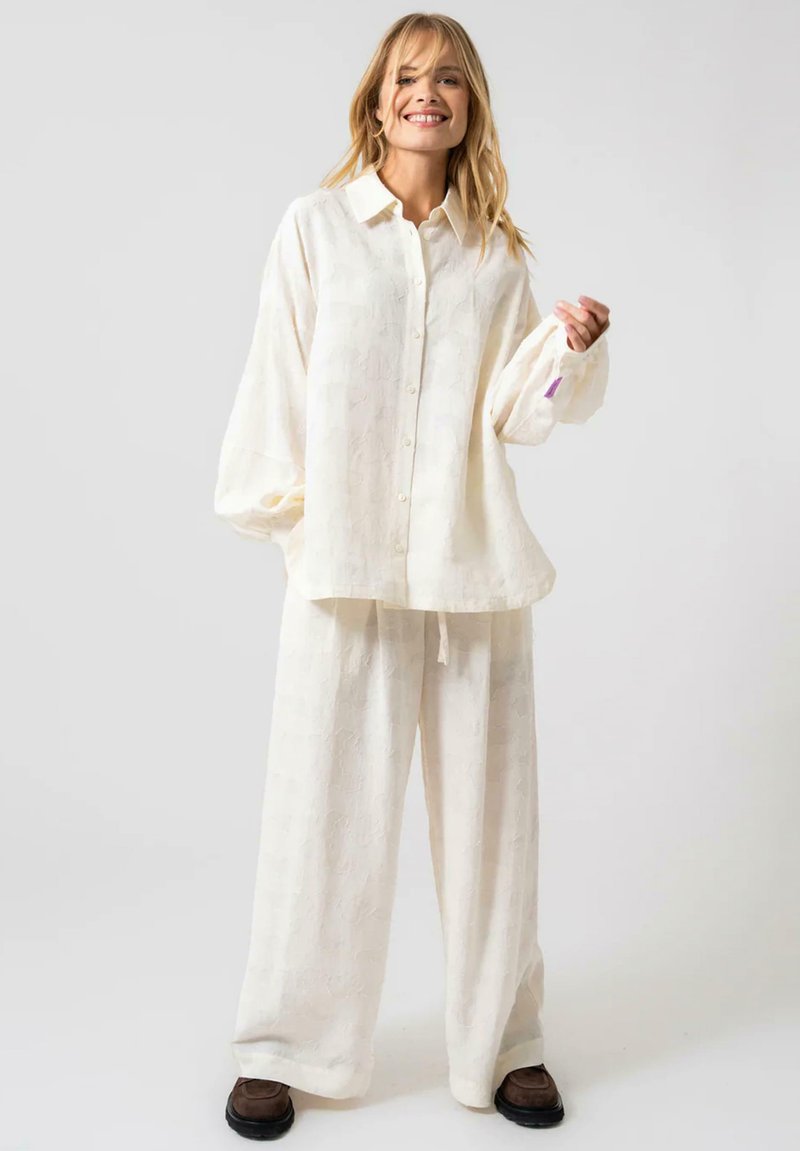 Crèmekleurig, losvallend linnen shirt en broek set met een subtiele textuur en knoopsluiting, met wijde mouwen en een strikceintuur.