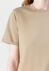 Kaki t-skjorte med kort erm laget av glatt bomullsstoff, med rund halslinning og oppbrettede mansjetter, med et enkelt og rent design.