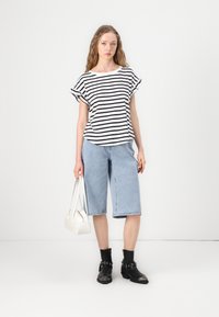 Striped, short-sleeve top in black and white; casual blue denim bermuda shorts; black ankle boots; white handbag. Simple, relaxed fit.
