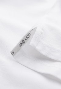 Tissu blanc texturé avec une étiquette de vêtement partiellement visible, montrant un texte imprimé à l'intérieur d'une couture pliée.