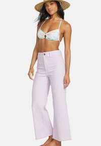 Licht lavendel hoge taille wijde jeans met franjes aan de onderkant, gecombineerd met een meerkleurige bikini top met een cirkelvormige uitsnijding.