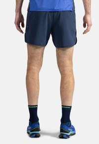 Marina shorts med sidofickor, gjorda av lättviktig tyg. Matchas med blå skor och svarta strumpor med gröna detaljer.