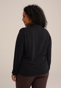 Maglietta nera a maniche lunghe con colletto, caratterizzata da una texture liscia e polsini abbottonati. La parte posteriore presenta una vestibilità comoda.