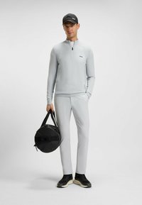 Maglione grigio chiaro con zip a 1/4, pantaloni abbinati, sneakers nere e una borsa da viaggio rotonda nera. Texture liscia, design minimalista, dettagli di marca.